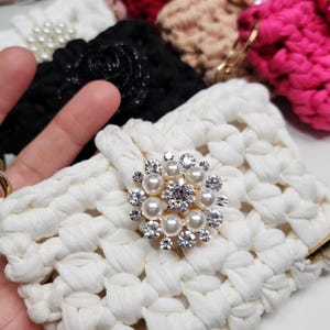 Puede incluir: Una colección de diademas hechas a mano en varios colores, incluyendo blanco, negro, rosa y burdeos. La diadema blanca presenta un adorno decorativo de perlas y pedrería. Otras diademas tienen adornos florales o de joyas.