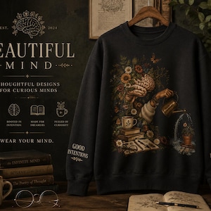 May include: A dark charcoal sweatshirt featuring a graphic of a human brain blooming with flowers, a hand watering a potted plant, books, and a coffee cup. The text "GOOD INTENTIONS" is on the right sleeve and "POOR DELIVERY" is on the left sleeve.