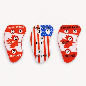 Peut inclure: Trois indicateurs de score de baseball sur fond blanc. Deux présentent une feuille d'érable rouge et les mots "OUT" et "INNING". Celui du centre a des rayures rouges et blanches et un champ d'étoiles bleu. Chaque indicateur affiche les comptes de balles, de prises et de manches.