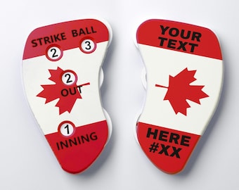 May include: Two white and red baseball umpire indicators featuring a Canadian maple leaf design. The left indicator displays STRIKE, BALL, OUT, and INNING with numbered dials. The right indicator features the text YOUR TEXT HERE #XX.
