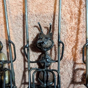 May include: Close-up of three metal ant sculptures. Each ant has a body made of a round, textured material and is supported by a metal frame. The ants have metal antennae and are welded together.