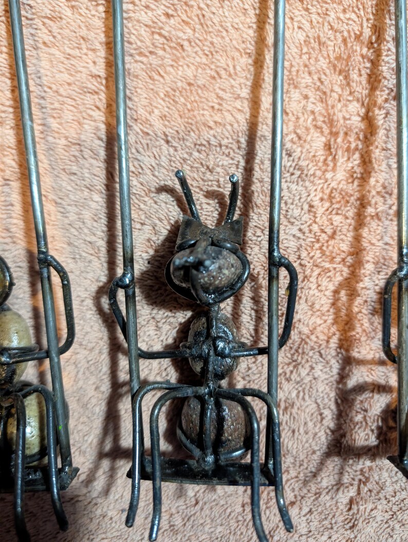 May include: Close-up of three metal ant sculptures. Each ant has a body made of a round, textured material and is supported by a metal frame. The ants have metal antennae and are welded together.