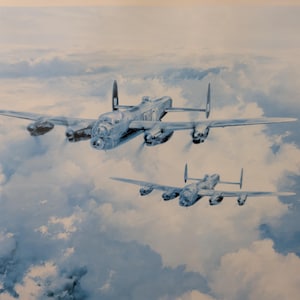 May include: A framed print of two Lancaster bombers flying through a cloudy sky. The artwork is primarily blue and white, with the planes in the foreground and clouds in the background. Text at the bottom includes the title "The Lancaster's T.C.'s".