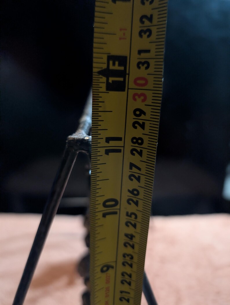 May include: A close-up of a metal object with a yellow measuring tape. The tape shows a measurement of approximately 10 inches. The object appears to be a decorative piece or part of a larger structure.
