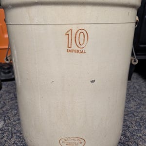 Può includere: Un boccale in ceramica beige con corpo arrotondato e bordo leggermente svasato. Il numero "10" e la parola "IMPERIAL" sono stampati in marrone. Il boccale ha manici in metallo e un timbro di Medalta Potteries Ltd.