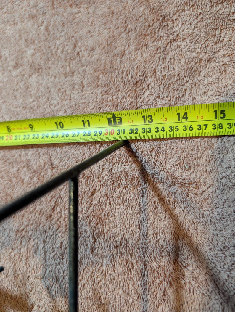 May include: A close-up of a yellow measuring tape with black markings, showing measurements in inches. The tape is positioned near a dark metal object. The background is a textured, light brown surface.
