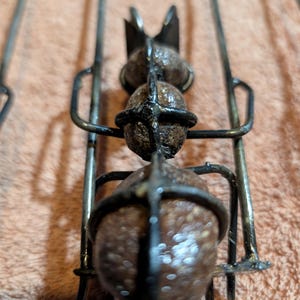 May include: Close-up of a metal skewer with three round, brown objects held in place by a metal cage. The skewer has a decorative top and is designed for grilling or roasting food.