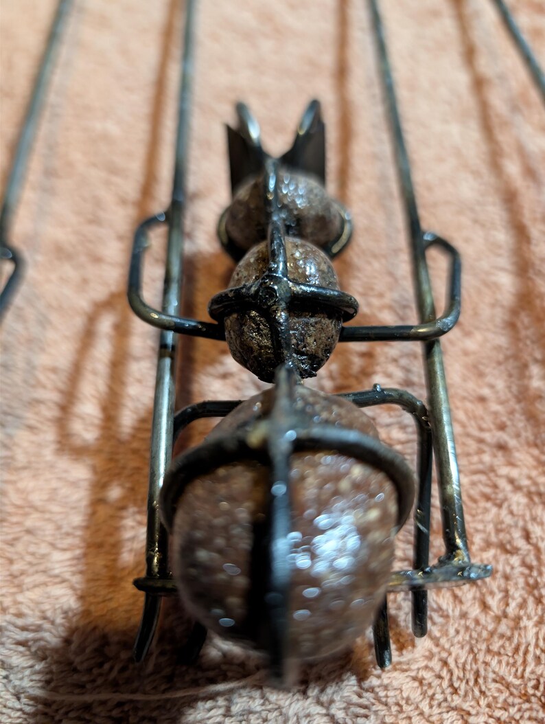 May include: Close-up of a metal skewer with three round, brown objects held in place by a metal cage. The skewer has a decorative top and is designed for grilling or roasting food.