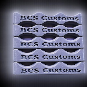 May include: Stacked, light gray custom-made holders with a wavy top edge. Each holder has the text "BCS Customs" engraved on it. The holders are arranged vertically, with a gradient background.