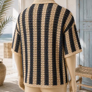 May include: A short-sleeved shirt featuring a vertical striped pattern in alternating dark navy blue and beige colors. The garment is constructed with an open-knit crochet texture, a standard collar, and a straight hemline, displayed on a mannequin.