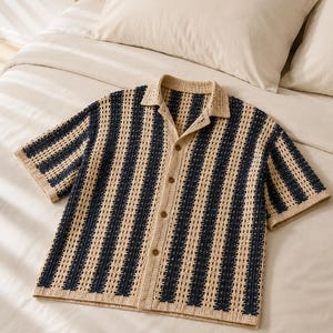 May include: A short-sleeved button-down shirt featuring a vertical striped pattern in navy blue and beige. The garment is constructed with an open-knit crochet texture, a classic collar, and four brown buttons running down the center front placket.