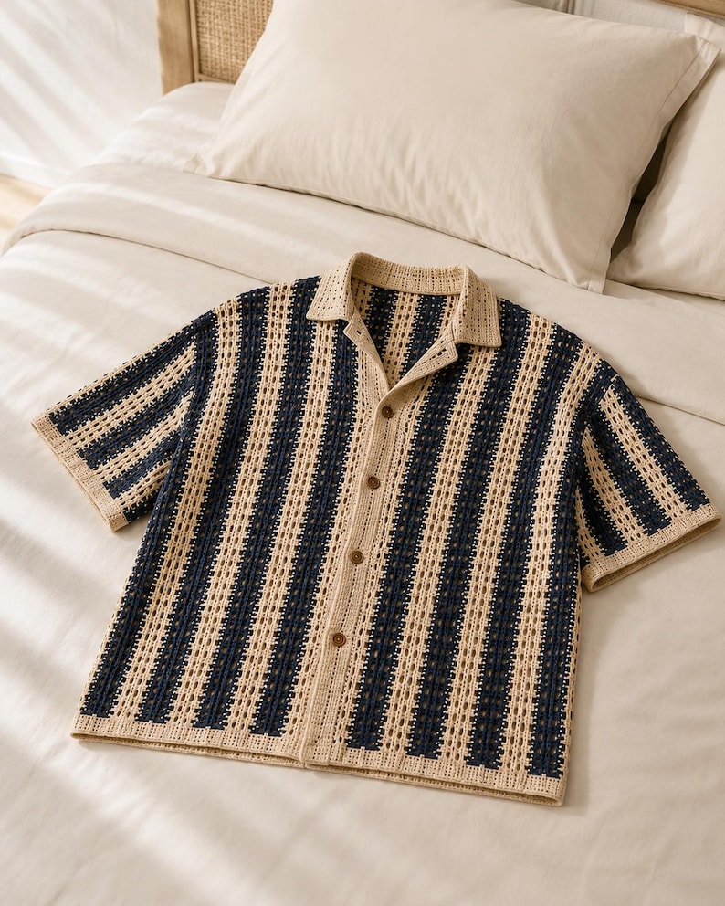 May include: A short-sleeved button-down shirt featuring a vertical striped pattern in navy blue and beige. The garment is constructed with an open-knit crochet texture, a classic collar, and four brown buttons running down the center front placket.