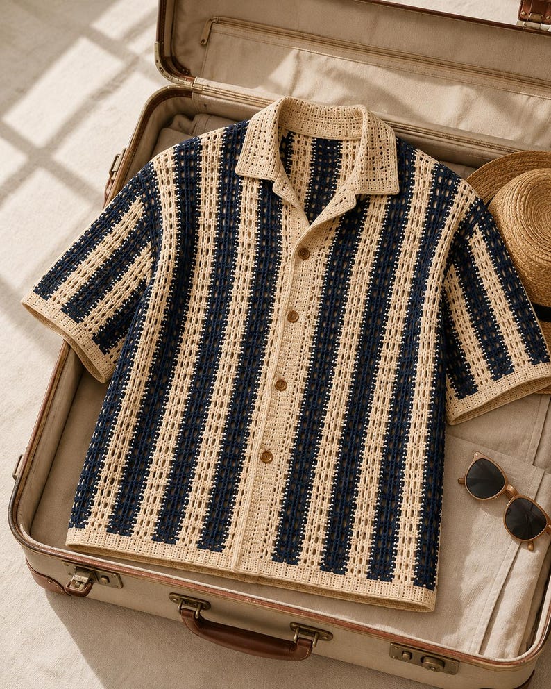 May include: A short-sleeve button-down shirt featuring a vertical striped pattern in navy blue and beige. The garment is constructed with an open-knit crochet texture, a classic collar, and four brown buttons running down the center front placket.