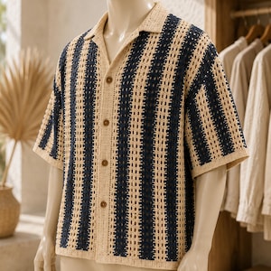 May include: A short-sleeved button-down shirt featuring a vertical striped pattern in navy blue and beige. The garment is constructed with an open-knit crochet texture, a classic collar, and four brown buttons down the center front placket.
