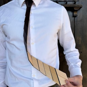 Peut inclure: Une cravate en bois au design unique. Elle est composée de pièces rectangulaires en bois, passant du marron foncé au marron clair. Portée avec une chemise blanche et un pantalon gris.