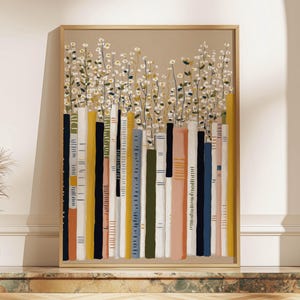 Whimsical art print of colorful vertical book spines with white daisies on a beige background, framed on a marble ledge beside a small vase and dried grasses.