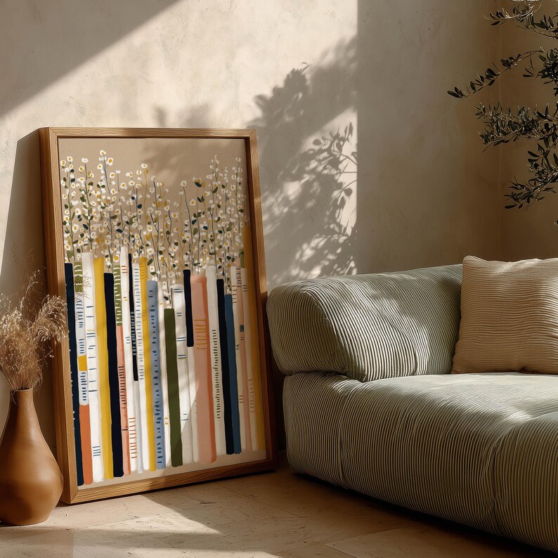 Atmospheric wall art print of vertical books and scattered white blossoms, leaning beside a textured sofa with dramatic shadows and a sculptural vase.