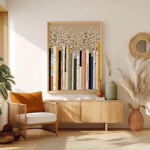 Neutral-toned bookshelf and daisy wall art print with vertical colorful spines, displayed above a light wood sideboard with pampas stems and a woven chair.