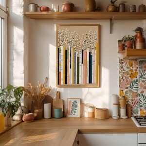 Warm bookshelf poster featuring multicolor book spines and delicate daisies, hanging above a wooden kitchen counter with open shelves, jars, and plants.