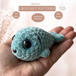 Puede incluir: Un peluche de foca tejido a ganchillo en color azul claro con grandes ojos de seguridad negros y una pequeña nariz negra. La imagen incluye el texto Mini Seal CROCHET PATTERN, NO SEW, BEGINNER FRIENDLY, PDF ONLY y el logo de hook hugs.