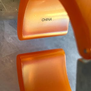 Pu&ograve; includere: Braccialetto a cerchio arancione incernierato. L'interno del braccialetto &egrave; di una tonalit&agrave; di arancione pi&ugrave; chiara. La parola "CHINA" &egrave; stampata all'interno del braccialetto.