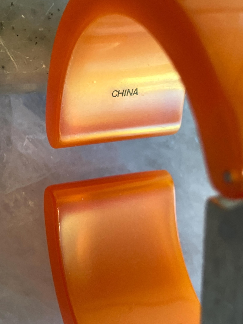 Pu&ograve; includere: Braccialetto a cerchio arancione incernierato. L'interno del braccialetto &egrave; di una tonalit&agrave; di arancione pi&ugrave; chiara. La parola "CHINA" &egrave; stampata all'interno del braccialetto.