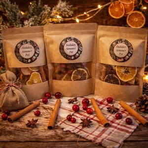 May include: Three brown paper bags with clear windows, each labeled "Holiday Simmer Pot," filled with dried fruit and spices. Cinnamon sticks, star anise, and cranberries are scattered on a wooden surface with a red and white checkered cloth.