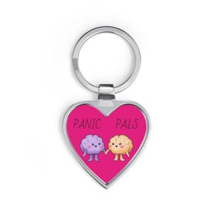 May include: Heart-shaped keychain with a silver metal frame and ring. The center features a bright pink background with the words "PANIC PALS" in black. Two cartoon brains, one purple and one yellow, are holding hands.