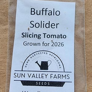 May include: A clear plastic bag containing Buffalo Solider Slicing Tomato seeds. The white label reads "Buffalo Solider Slicing Tomato Grown for 2026" with a logo and "Sun Valley Farms Seeds Woodbury, Tn."