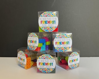 May include: Clear plastic boxes filled with colorful building blocks. Each box has a circular label that reads "WE WERE BUILT TO BE FRIENDS! FROM, JEFFERY" in a playful font, surrounded by a confetti-like design.