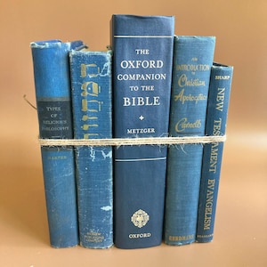 May include: A stack of five blue hardcover books bound together with a single strand of tan twine. The titles include Types of Religious Philosophy, The Oxford Companion to the Bible, An Introduction to Christian Apologetics, and New Testament Evangelism.