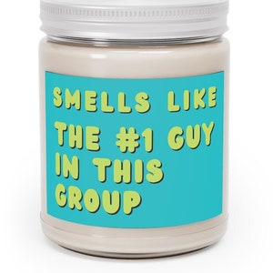 May include: A white candle jar with a teal blue label that says "Smells Like The #1 Guy In This Group" in yellow text.
