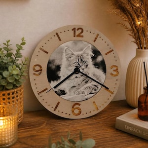 Könnte beinhalten: Runde Wanduhr aus Holz mit einem Schwarz-Weiß-Bild einer Katze. Die Uhr hat goldfarbene Ziffern und Zeiger. Die Uhr hat einen Durchmesser von etwa 25 cm.