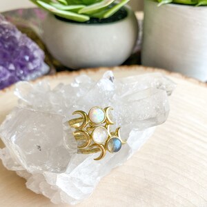 May include: Three gold rings with crescent moon designs and gemstone accents. The rings feature a white opal, a white moonstone, and a blue labradorite.
