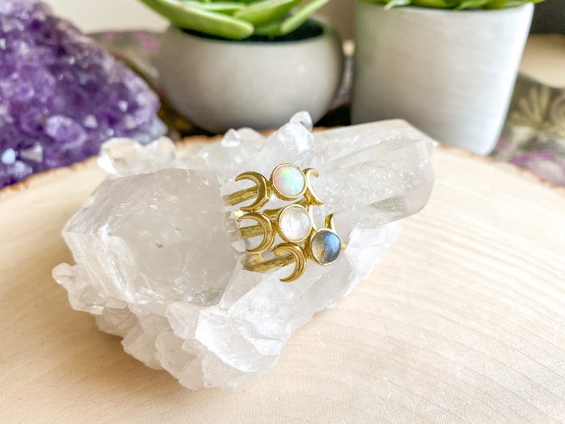 May include: Gold ring with three crescent moons and three gemstones: a white opal, a white moonstone, and a blue labradorite.