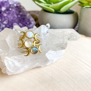 May include: Three gold rings with crescent moon designs and different colored gemstones. The rings are stacked on top of each other and are sitting on a white crystal cluster.