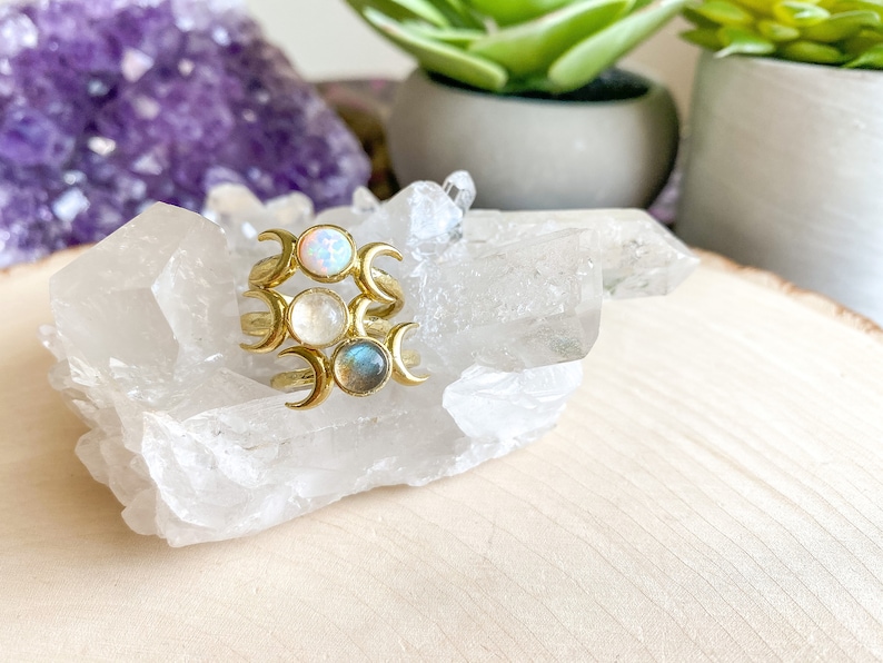 May include: Three gold rings with crescent moon designs and different colored gemstones. The rings are stacked on top of each other and are sitting on a white crystal cluster.