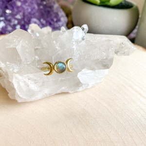 May include: Gold ring with a triple moon design and a blue-green labradorite gemstone.