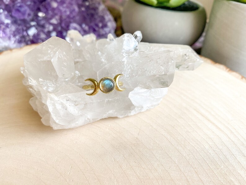 May include: Gold ring with a triple moon design and a blue-green labradorite gemstone.