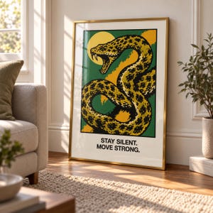 Puede incluir: Una lámina de arte enmarcada que muestra una serpiente con patrón amarillo y negro con la boca abierta sobre un fondo verde y amarillo. Debajo de la ilustración, el texto dice: STAY SILENT. MOVE STRONG. La lámina tiene un marco dorado fino.