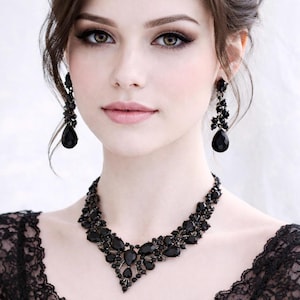 May include: A woman wearing a black beaded necklace and matching earrings. The jewelry features teardrop-shaped pendants and intricate detailing. She is wearing a black lace top. The image is a close-up portrait.