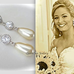 May include: Elegant silver-toned drop earrings with clear, sparkling crystals and pear-shaped faux pearls. The earrings are displayed next to a smiling woman in a wedding dress. The text "Queen Me Jewlery" is visible.