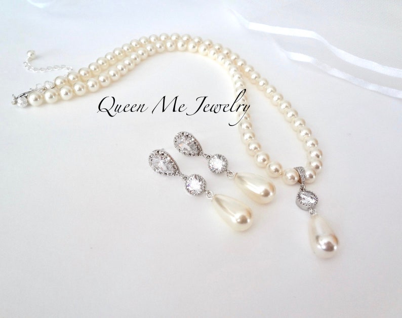 May include: A pearl necklace and matching earrings set. The necklace and earrings feature cream-colored pearls and sparkling clear crystals. The earrings have a teardrop pearl pendant. The text "Queen Me Jewelry" is visible.