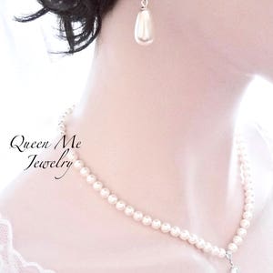 May include: Elegant pearl necklace and matching earrings. The necklace features a strand of small, round pearls with a delicate pendant. The earrings have a teardrop pearl and sparkling accents. The text "Queen Me Jewelry" is visible.