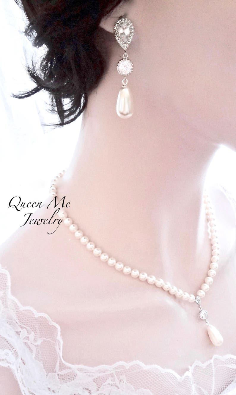 May include: Elegant pearl necklace and matching earrings. The necklace features a strand of small, round pearls with a delicate pendant. The earrings have a teardrop pearl and sparkling accents. The text "Queen Me Jewelry" is visible.
