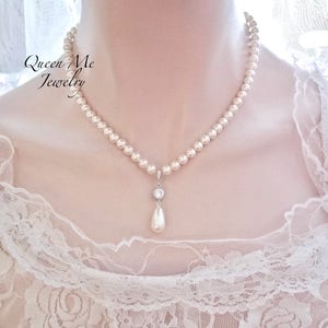 May include: A pearl necklace with a pendant. The necklace features a strand of small, round pearls. The pendant has a small, round, clear stone setting with a pear-shaped pearl drop. The text "Queen Me Jewelry" is in the upper left corner.