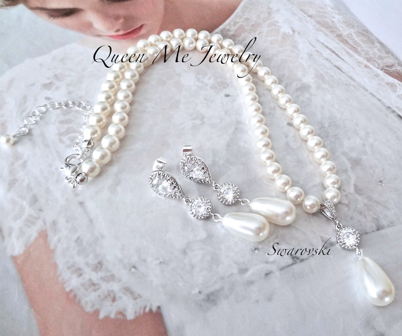 May include: A pearl necklace and matching earrings set. The necklace features multiple strands of white pearls with a silver clasp. The earrings have a teardrop pearl design with clear crystals. The set is labeled "Queen Me Jewelry" and "Swarovski".