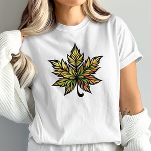 Op de afbeelding: Wit T-shirt met een kleurrijk, gestileerd bladontwerp. Het blad heeft een gedetailleerde, meerkleurige uitstraling met tinten groen, geel en oranje, omlijnd in zwart. Een casual kledingstuk voor dagelijks gebruik.
