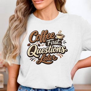 Puede incluir: Camiseta blanca con un diseño temático de café. El diseño presenta el texto "Coffee First, Questions Later" en letras marrones y beige, junto con granos de café y una taza de café humeante.