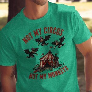 May include: Green t-shirt with the text "NOT MY CIRCUS NOT MY MONKEYS" in red. The shirt features a circus tent and three cartoon monkeys with bat wings. The monkeys are wearing purple and green hats.